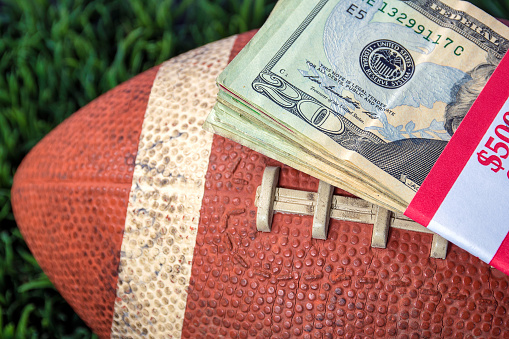 close up of wrapped money stack on football and green grass background